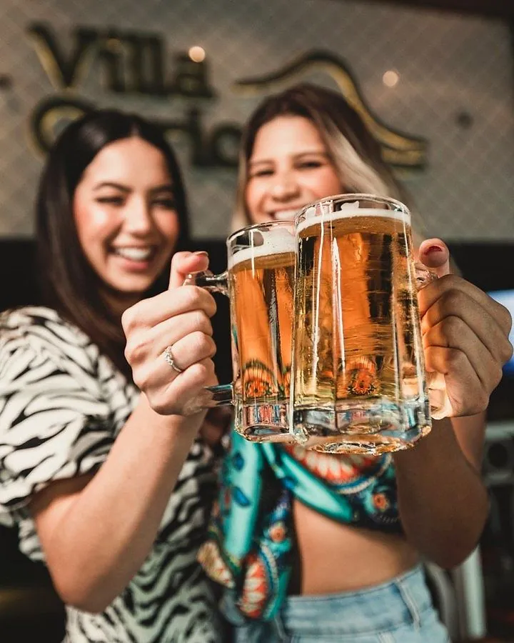 Duas amigas brindando com canecas de chopp no Villa Carioca