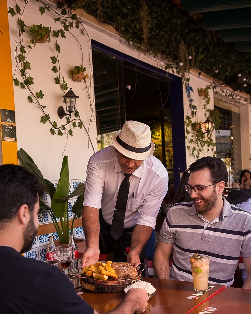 Garçom do Villa Carioca de chapéu branco servindo uma mesa